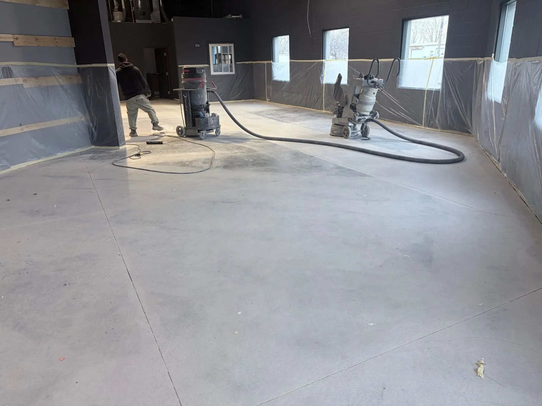 Crew grinding a concrete floor with dust extraction and protected walls in a commercial gym in Blaine, MN